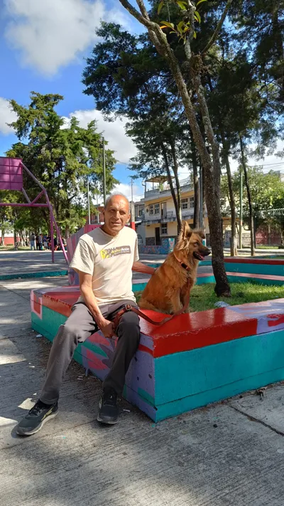 Vecino sentado con su perro en una banca pintada del parque, zona 7