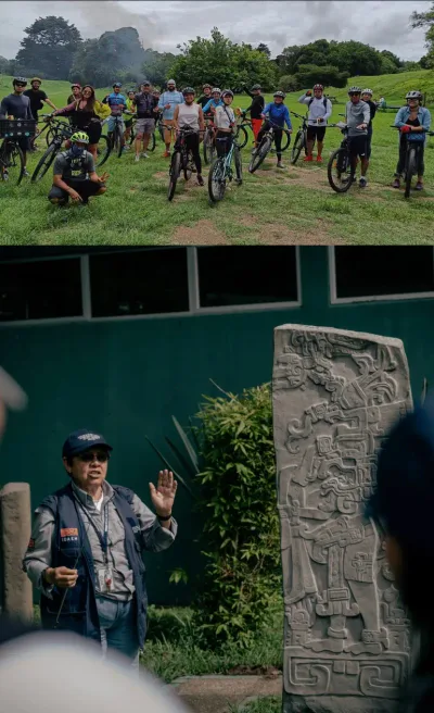 Grupo de ciclistas en un campo verde y guía explicando junto a una estela tallada